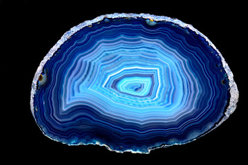 Slice of blue agate stone specimen, with rings of different blue shades, against a black limbo...
