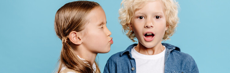 panoramic shot of kid kissing shocked friend isolated on blue