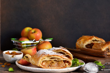 Apple strudel with cinnamon, nuts and and raisins on a dark concrete background.