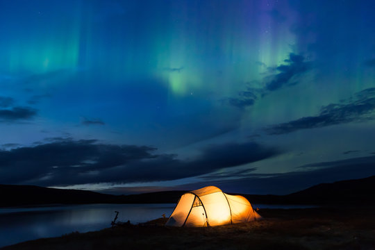 Northern lights dancing over an iluminated tent in Norway