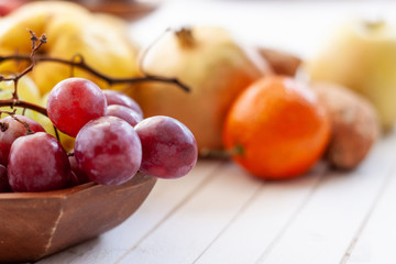 Fall fruits, like grapes,  close up over a wooden bowl with a white wooden background with copy space.