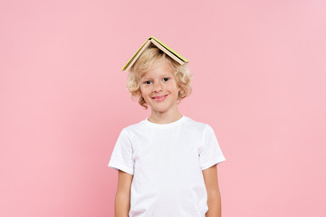 smiling kid with book on head isolated on pink
