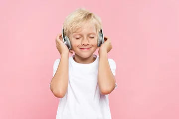 Tuinposter smiling kid with headphones listening music isolated on pink © LIGHTFIELD STUDIOS