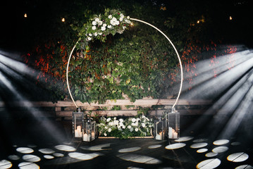 Evening ceremony. Beautiful wedding round arch decorated with flowers, greenery and candles,...