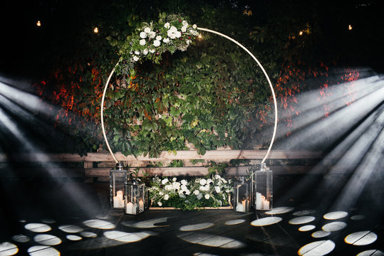 Evening ceremony. Beautiful wedding round arch decorated with flowers, greenery and candles, outdoors