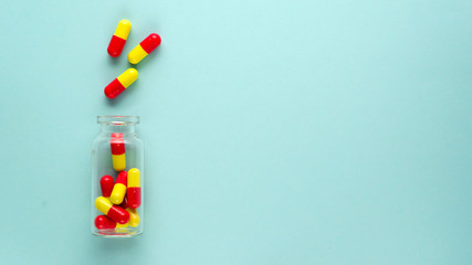 Bright red and yellow medicinal capsules in glass transparent bottle on a light blue background....