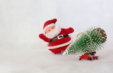 Toy Santa Claus on background blurred toy car carrying Christmas tree. Simulated snowy landscape. Space for text.