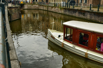 Fototapeta na wymiar Amsterdam, Netherlands. August 2019. Tourist boats explore the canals of the center continuously, in the photo a wooden cabin boat is about to pass under a bridge.