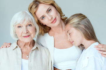 granddaughter with closed eyes, smiling mother, grandmother hugging isolated on grey
