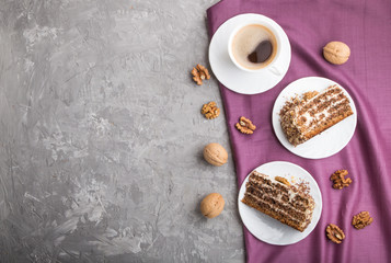 Homemade cake with milk cream and walnuts with cup of coffee on a gray concrete background, top view.