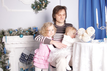 father with two daughters are sitting at a table in a room with New Year's decorations