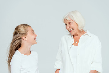 smiling granddaughter and grandmother looking at each other isolated on grey