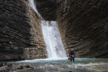 woman with canyoning costume inside the turquoise water of a waterfall in a mountain canyon