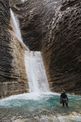 woman with canyoning costume inside the turquoise water of a waterfall in a mountain canyon. Vertical
