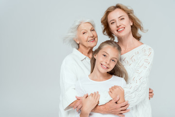 smiling granddaughter, mother and grandmother hugging isolated on grey