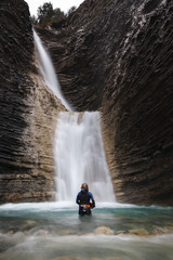 Woman in a canyoning costume in the turquoise water submerged to the waist of a waterfall in a mountain ravine. Long exposition. Vertical