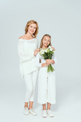 attractive mother hugging smiling daughter with bouquet on grey background