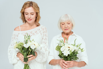 attractive mother and smiling daughter holding bouquets isolated on grey