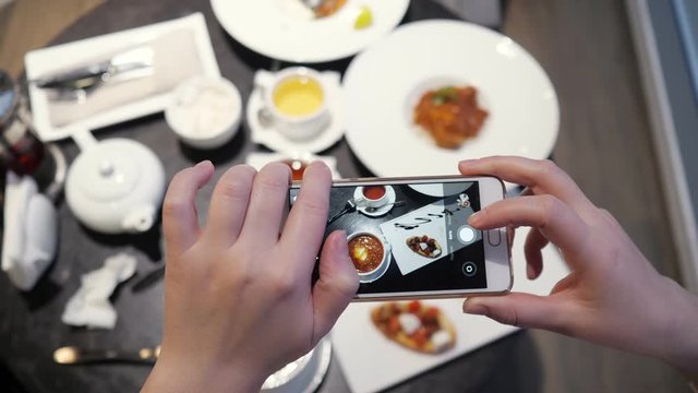 Woman takes pictures of food on the phone in a cafe, top view