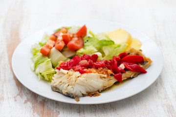 cod fish with red pepper, potato and salad on white plate on ceramic background