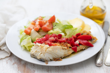 cod fish with red pepper, potato and salad on white plate on ceramic background