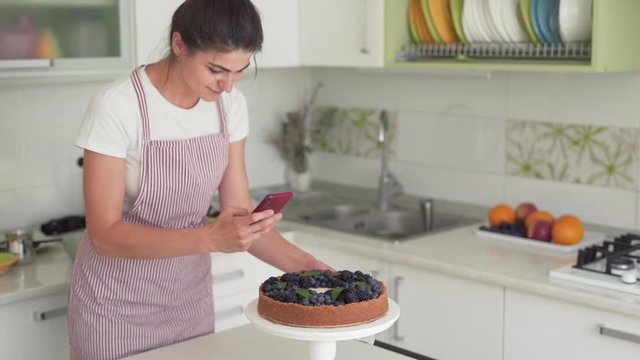 Close-up scene of a female cook who has just made a cheesecake and now has taking a photo of it on a phone.