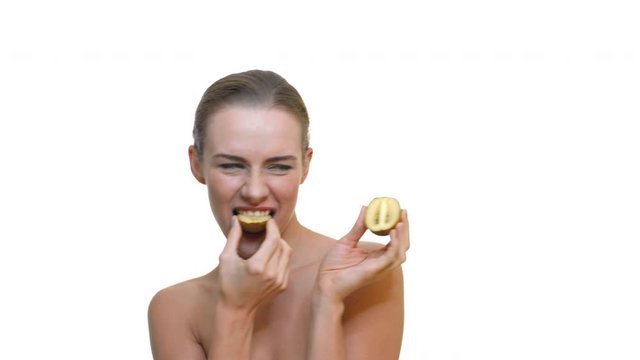 Beautiful woman eating ripe kiwi while topless on white background. Blonde girl happily eats citrus fruit on copy space