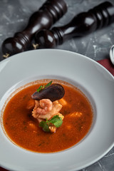 Fresh seafood soup in a white plate on dark background, top view