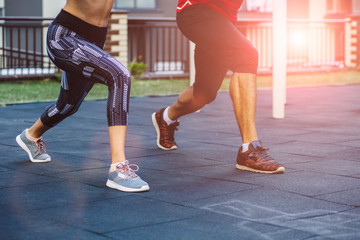 fitness, sport, exercise, lifestyle concept. Mixed race young man and woman doing exercise on street sports ground. Team of two athletes exercising lunges while having sports training in the morning.