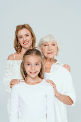 smiling mother, grandmother and granddaughter hugging isolated on grey