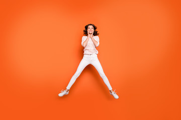 Fototapeta na wymiar Full size photo of positive cheerful girl have fun on spring time weekends jump touch face hands wear good looking clothing isolated over orange color background