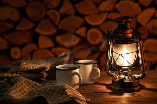  The antique oil lamp and cups with hot tea on the firewood background.