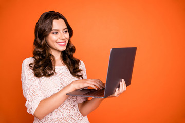 Portrait of positive cheerful girl use her computer have online conversation with friend on social media account wear good looking outfit isolated over orange color background