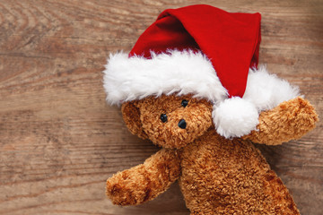 Teddy bear in Santa Claus hat. Plush toy on shabby wooden background. New Year.