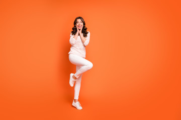 Full body photo of charming lovely girl enjoy free time look friend news scream wow omg touch hands face wear casual style clothing isolated over orange color background