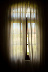 Window of an old house with curtains that let in a beautiful light.