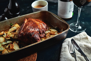 Roasted pork neck with baked potatoes and herbs on a tray on the black background