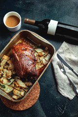 Roasted pork neck with baked potatoes and herbs on a tray on the black background