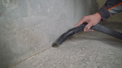 A worker vacuums a concrete floor. Worker washes the floor with a vacuum cleaner from industrial concrete dust and cement mud during home renovation