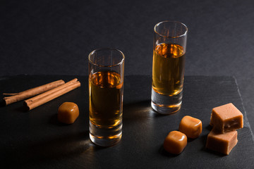 Glass of whiskey with caramel candies on a black stone slate board on black background. Side view,...