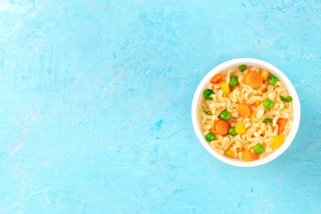Instant noodles with vegetables in a plastic cup, overhead shot on a blue background with a place...