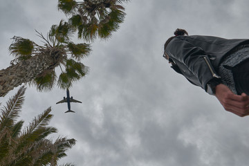 low angle of a boy watching a plane between palm trees