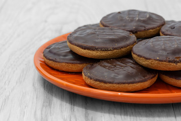 Jaffa cakes biscuits stacked on an orange plate.  On a grey wood surface.