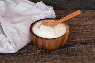 Natural homemade plain organic yogurt in wooden bowl and wood spoon on wood texture background