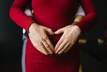 Expecting a baby. Hands of husband and wife on pregnant belly in red dress. Valentine's day
