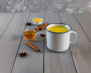 Golden milk, turmeric, honey, ginger root, cinnamon and other ingredients on grey wooden...