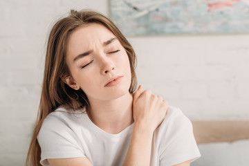frowned girl with closed eyes touching neck while suffering from pain