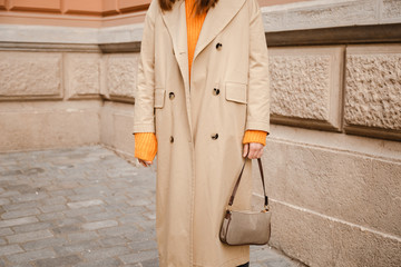 street style details. an attractive woman wearing a beige trench coat and 90s pattern vintage shoulder mini bag, crossing the street. fashion outfit perfect for autumn