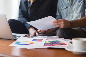 Architect and customer discussing floor plan. Closeup of human hands, laptop, swatches, coffee cups on table. Renovation or home decoration concept