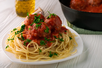 Close-up of spaghetti with meatballs with tomato sauce and parsley in white plate and black pan with meatballs